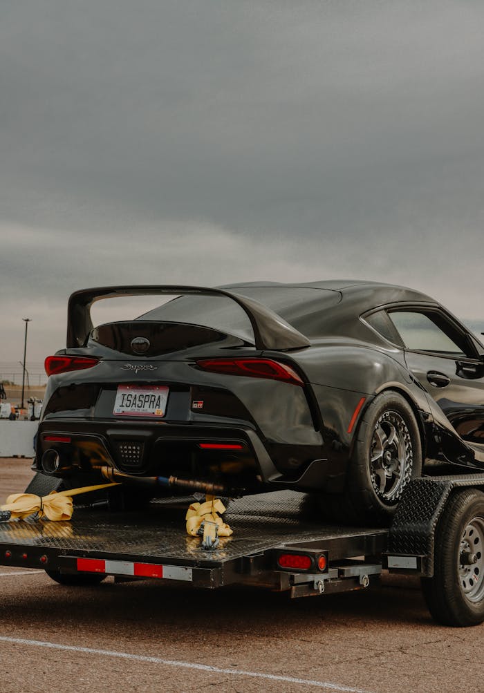 A sleek black sports car with a spoiler on a trailer, ready for transport outdoors.